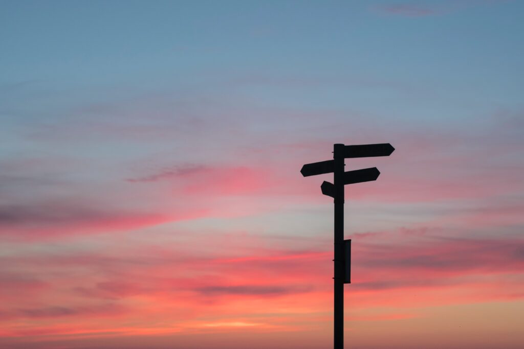 Photographie de paneaux indicateurs à contre-jour sur un fond de lever de soleil bleu et rose.