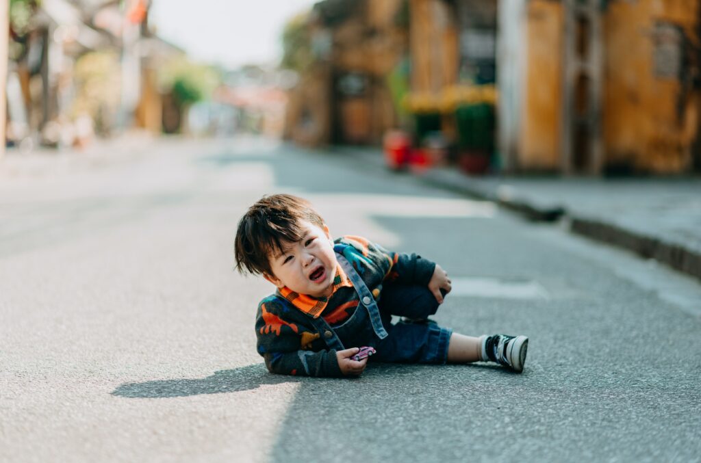 Photographie d'un petit garçon tombé dans la rue, une petite voiture à la main.
