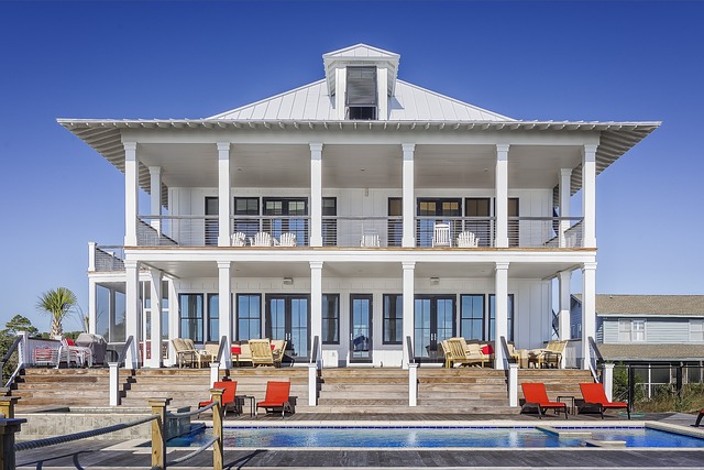 grande maison blanche en bois de style colonial avec terrasses, chaises longues et piscine.