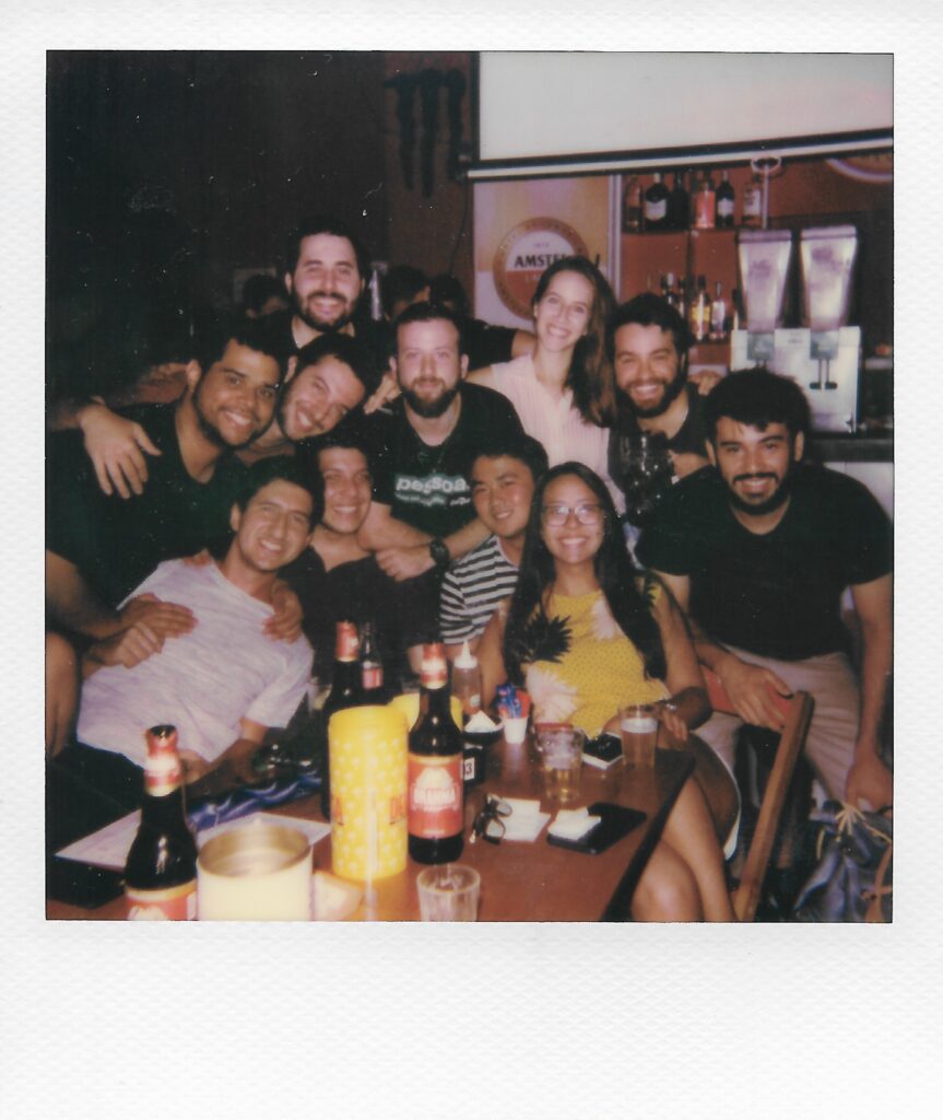 Groupe d'une dizaine de personnes, posant avec le sourire au bout d'une table sur laquelle sont posées des bouteilles.